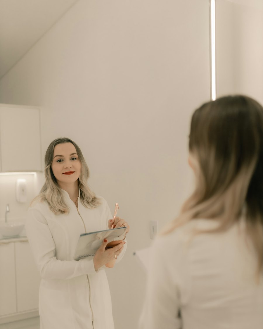 A clinician in a white coat holds a folder and pen, seen in a mirror in a bright, minimal clinic room