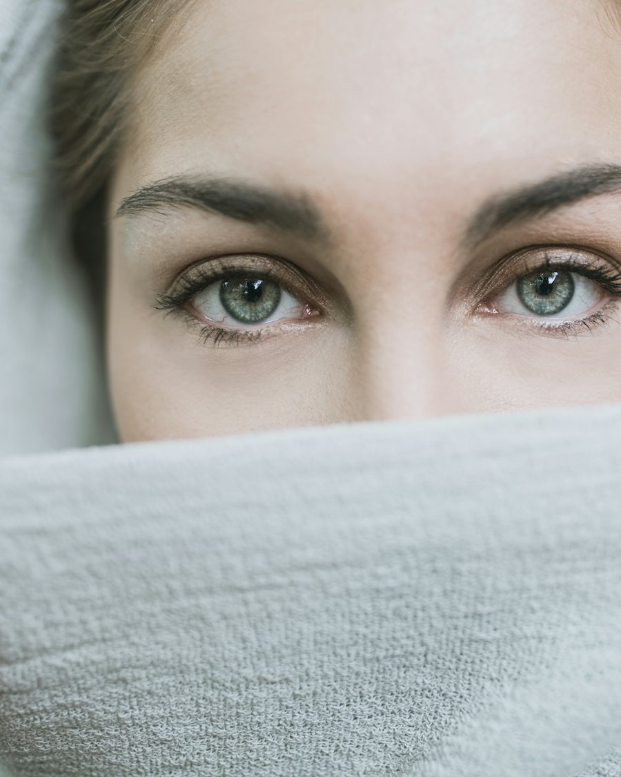 Close-up of a woman's green eyes and brows above a soft light gray towel